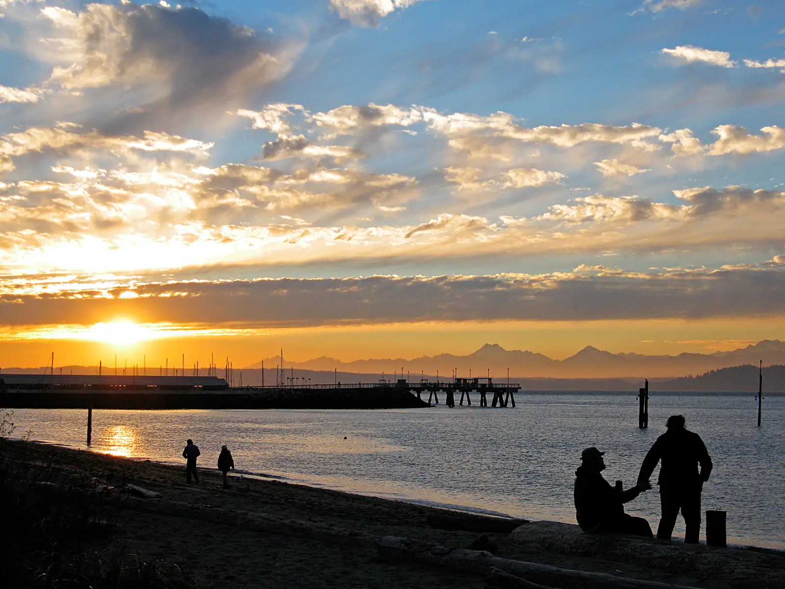 Sunset over Puget Sound and the Olympic Mountains from the Edmonds waterfront, with people walking along the beach
